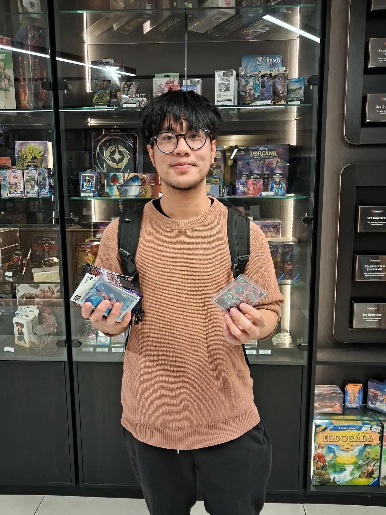 The qualifier winner at Černý Rytíř holding cards in front of the shop's display case